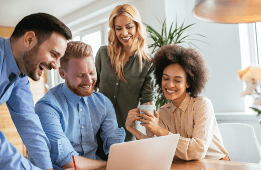 Four smiling educators gathered together and looking down at a laptop